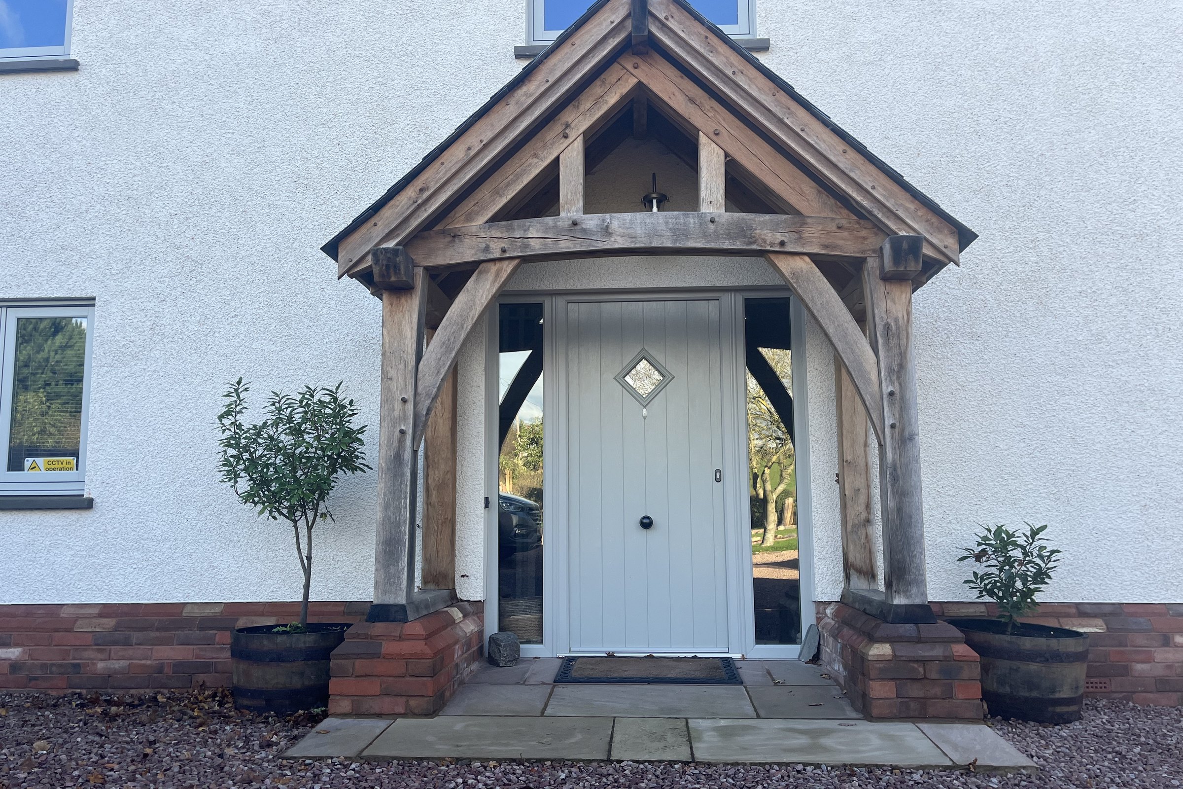 Silvered oak gable porch on red brick plinths in front of a white rendered house at Penpergwm