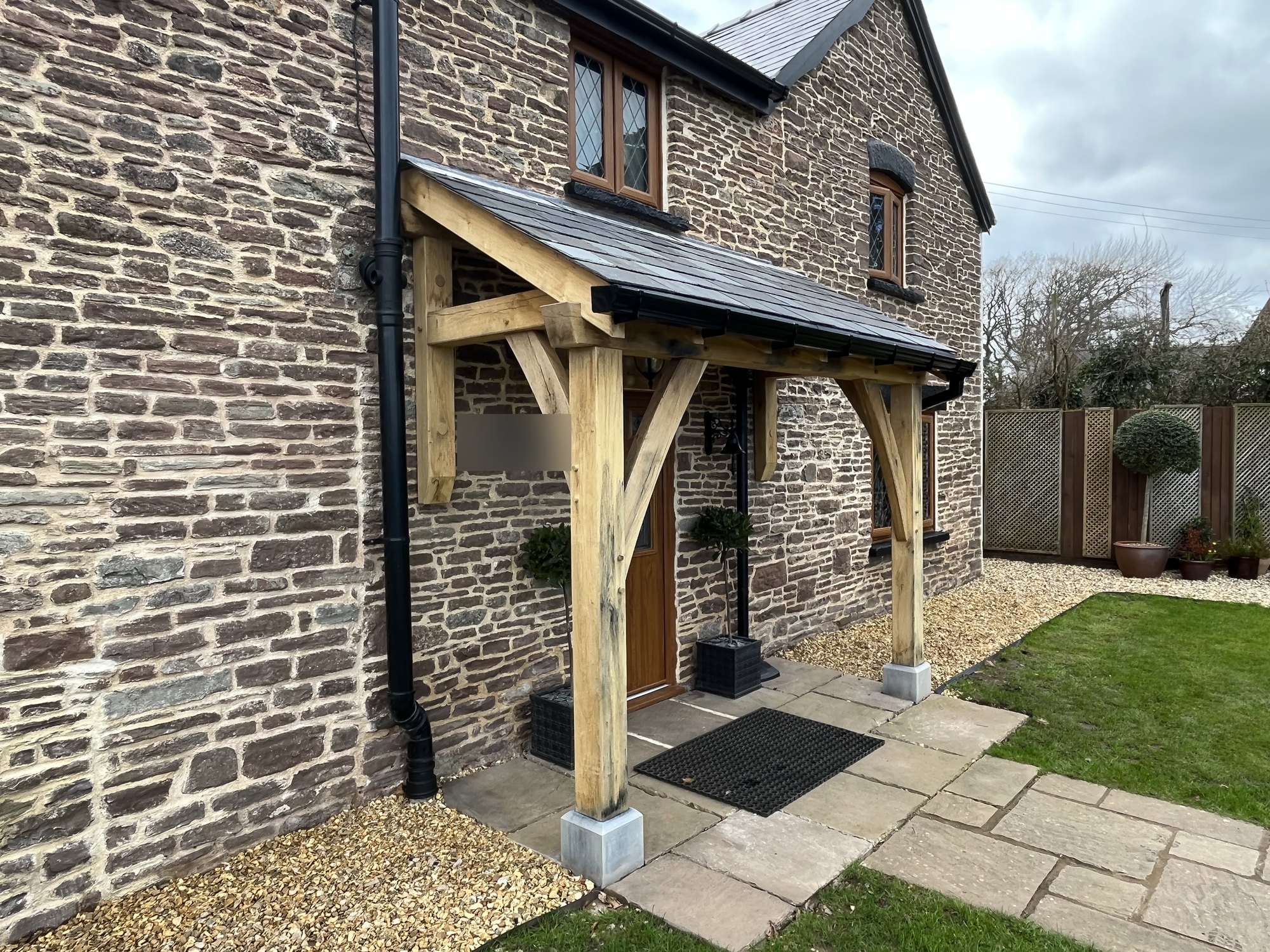 Oak lean-to porch on a stone cottage at Newcastle, near Monmouth, seen from the right over the existing flagstones
