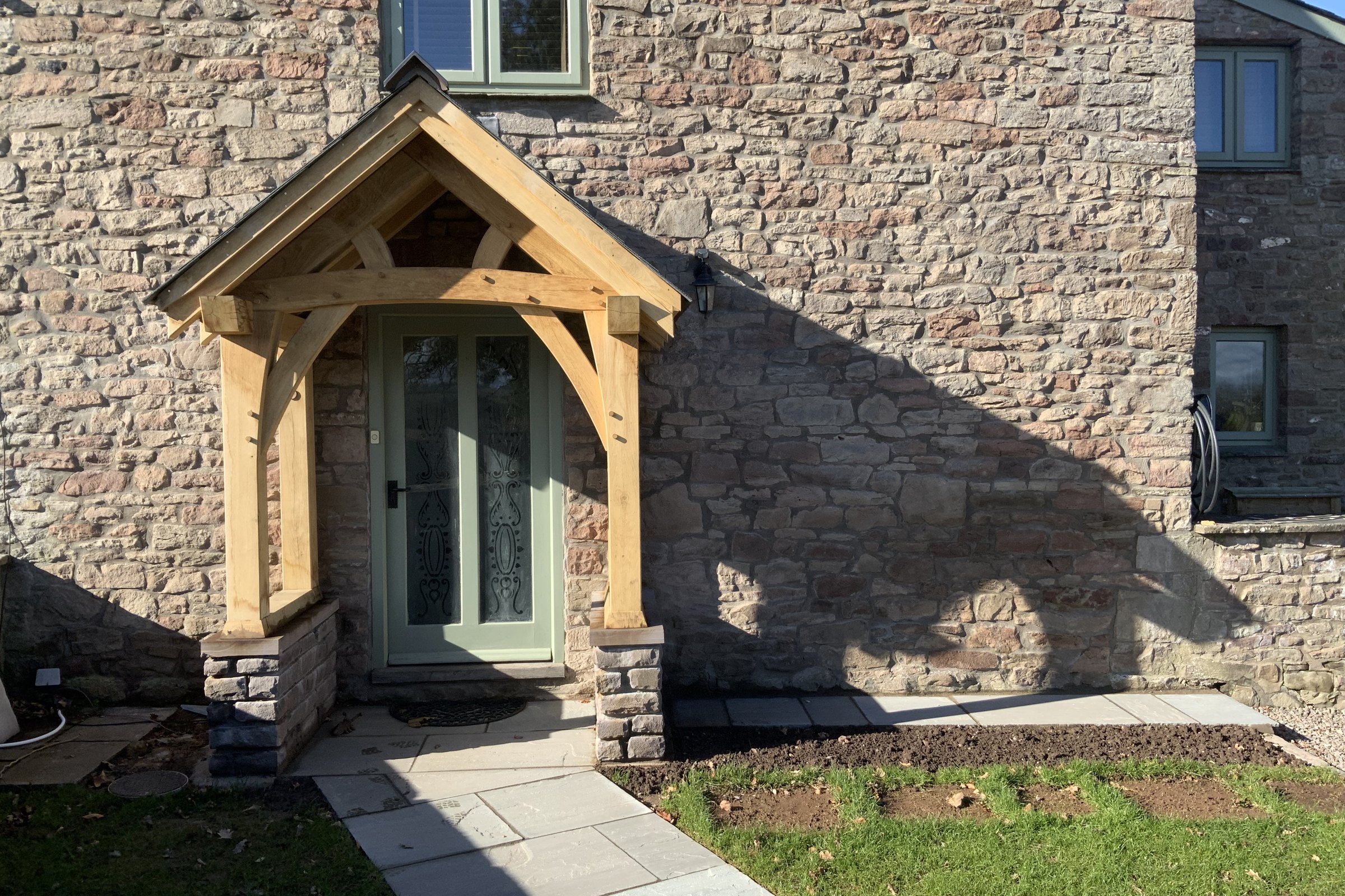 Oak frame porch on low stone plinth walls against a stone house at Llantilio Crossenny