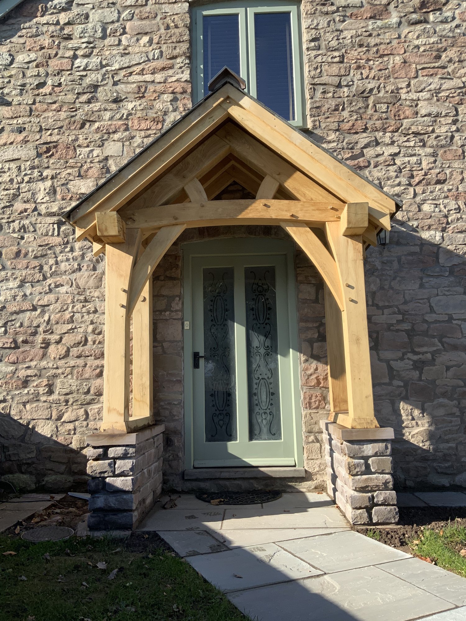 Straight-on view of an open oak porch, its posts standing on low stone plinth walls, at Llantilio Crossenny