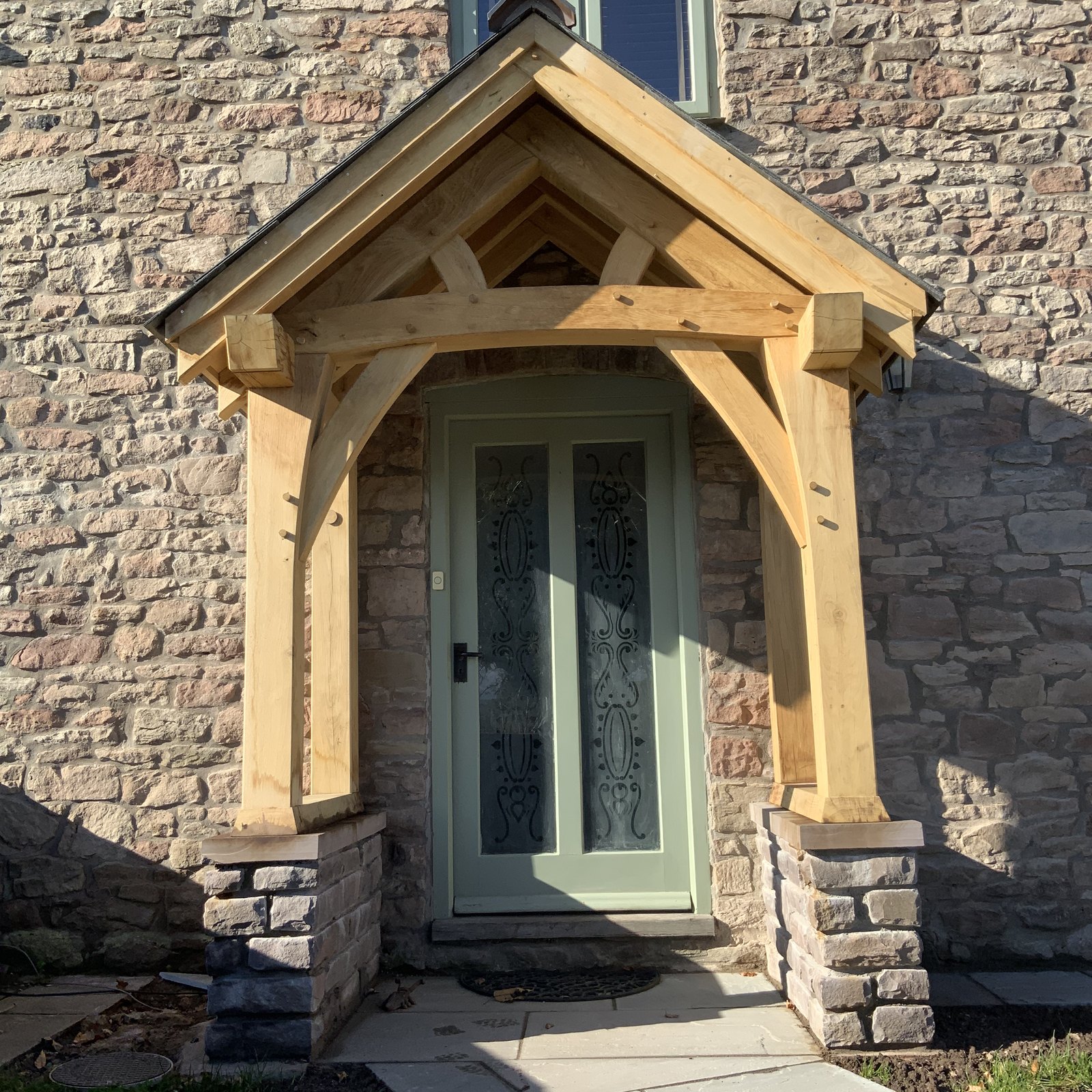 Oak porch with curved braces on stone plinths over a sage green door