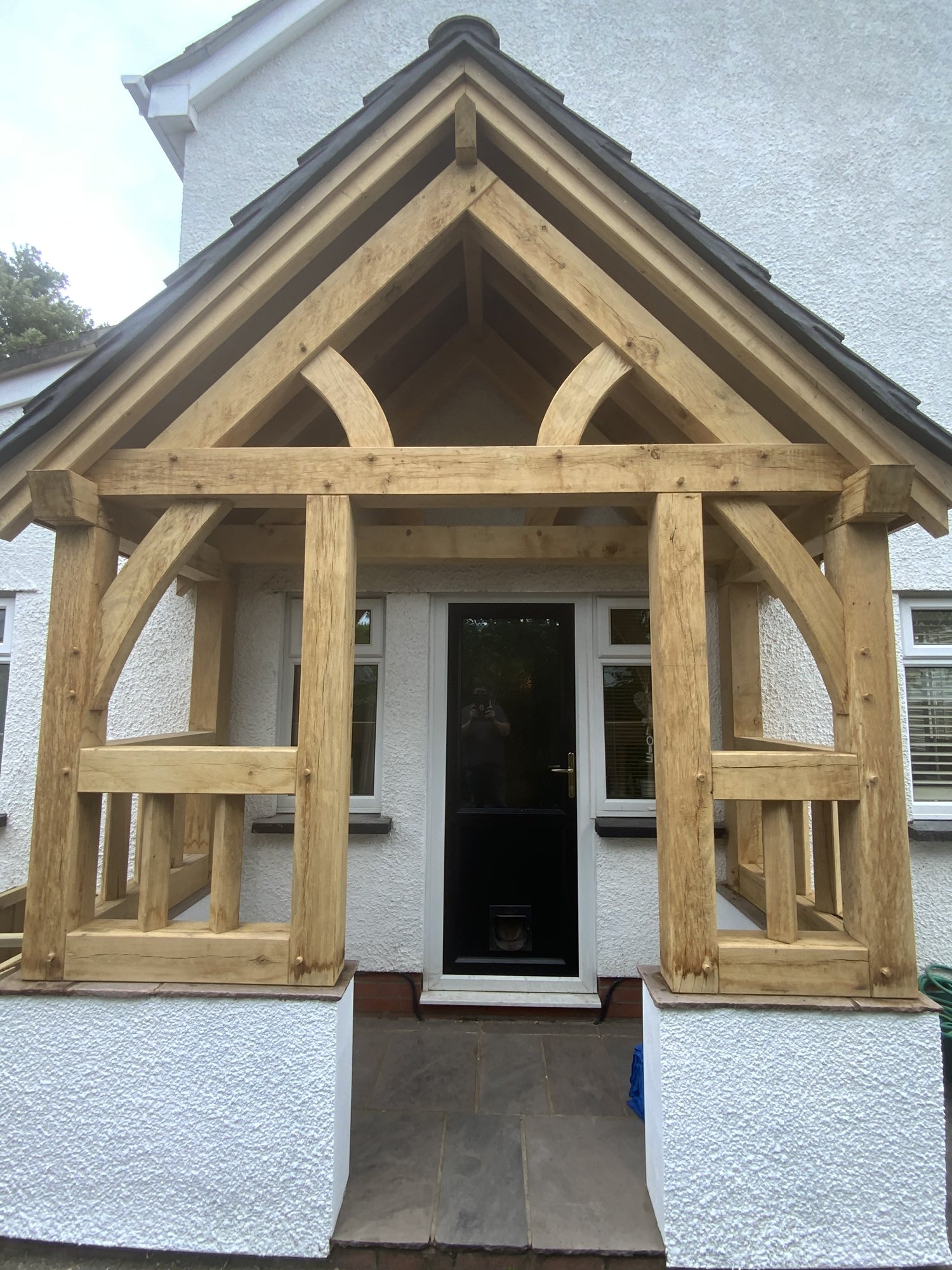 Straight-on view of an oak gable porch and its balustrade sides on a white rendered house in Abergavenny