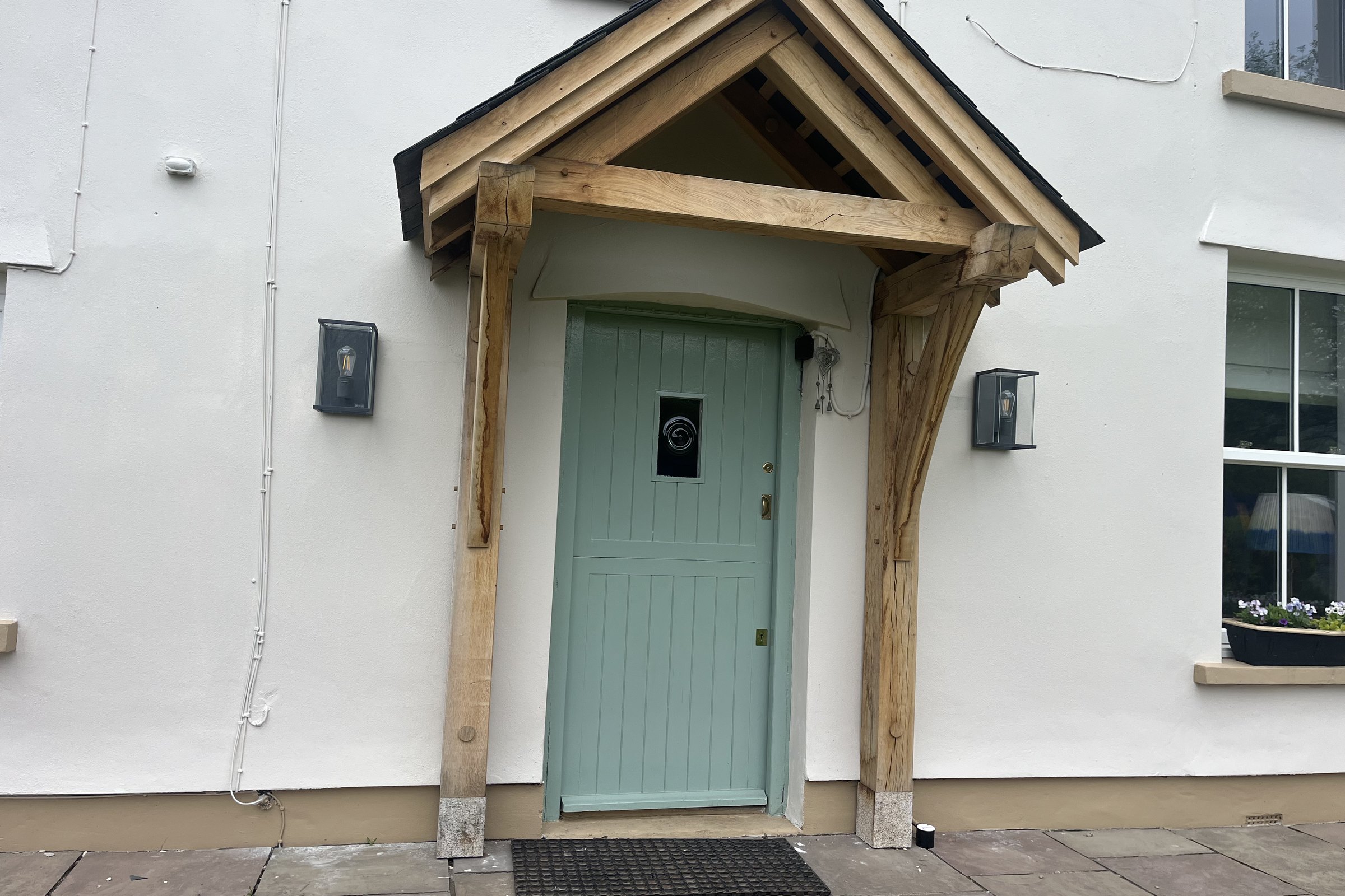 Oak gable porch over a pale green door on a white rendered house at Usk