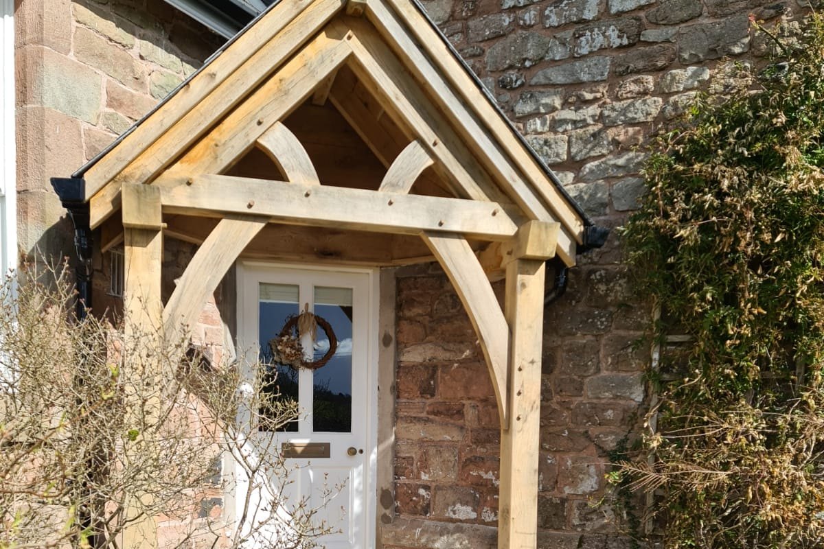 Oak gable porch over a white front door on a sandstone cottage at Catbrook