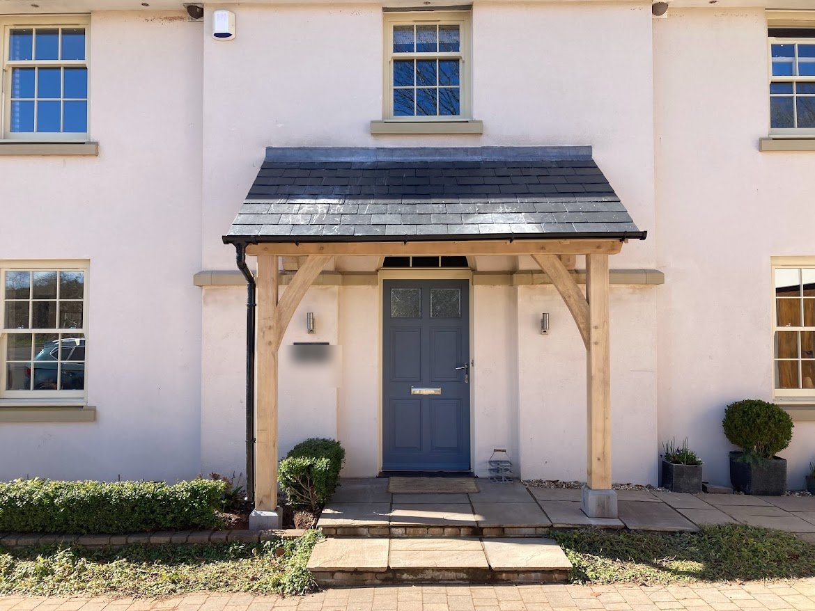 Open oak lean-to porch with a slate roof over a grey front door, Trellech