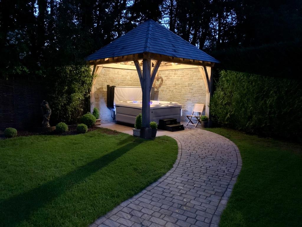 Oak frame gazebo with a cedar shingle roof over a hot tub, lit at dusk, Llanvihangel Crucorney