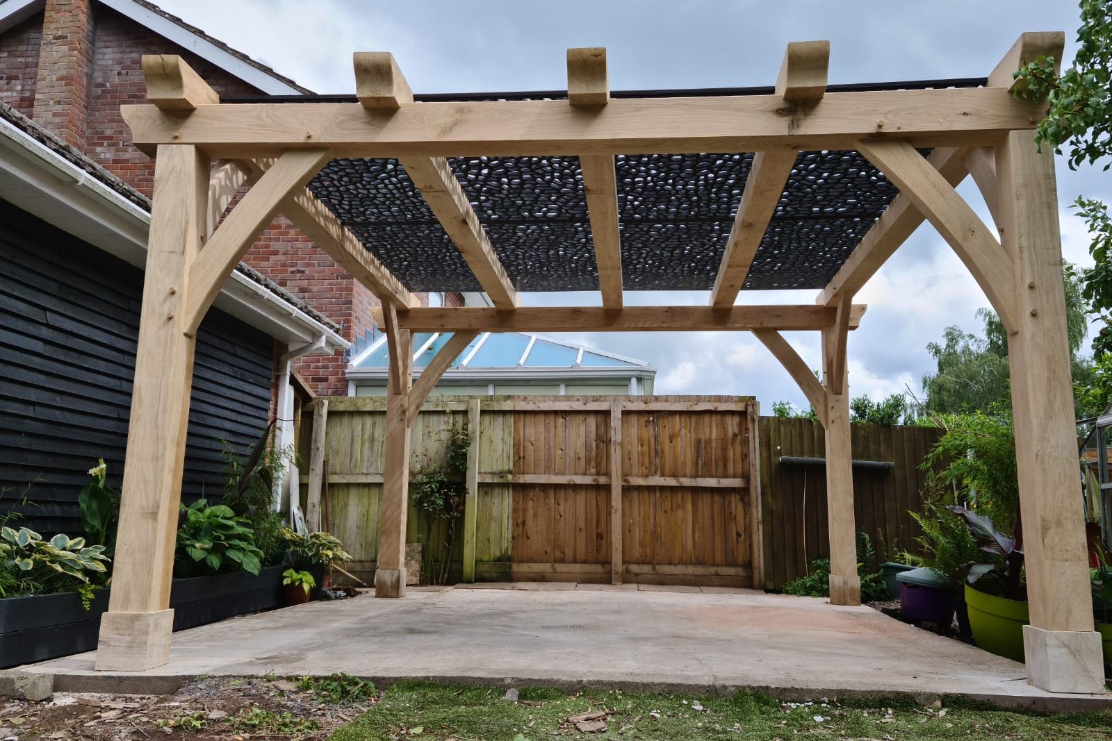 Oak pergola with curved braces and a patterned shade screen at Crickhowell