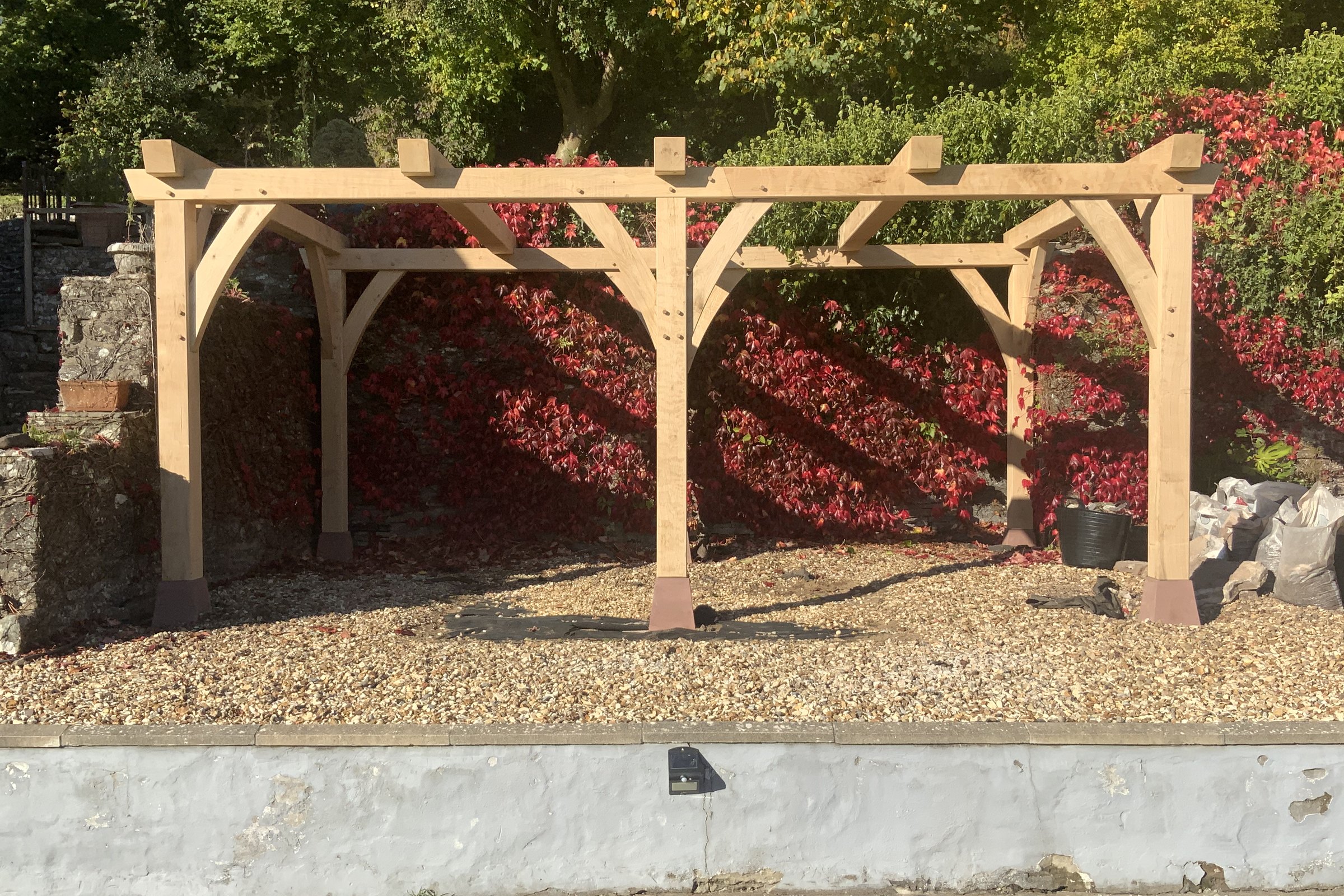 Oak pergola in front of a red creeper-covered wall at Bwlch