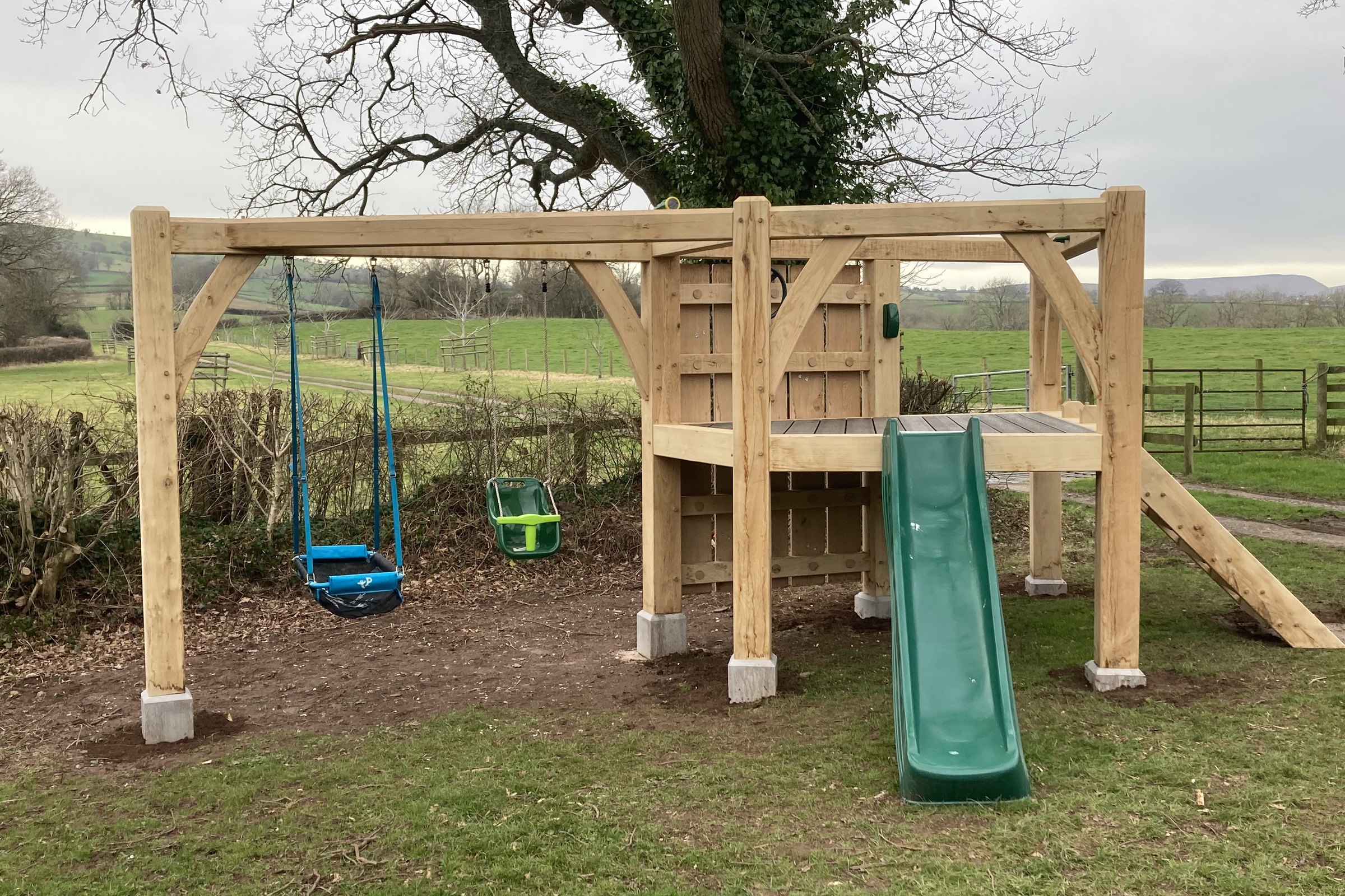 Oak play structure with swings, slide and climbing wall in a garden