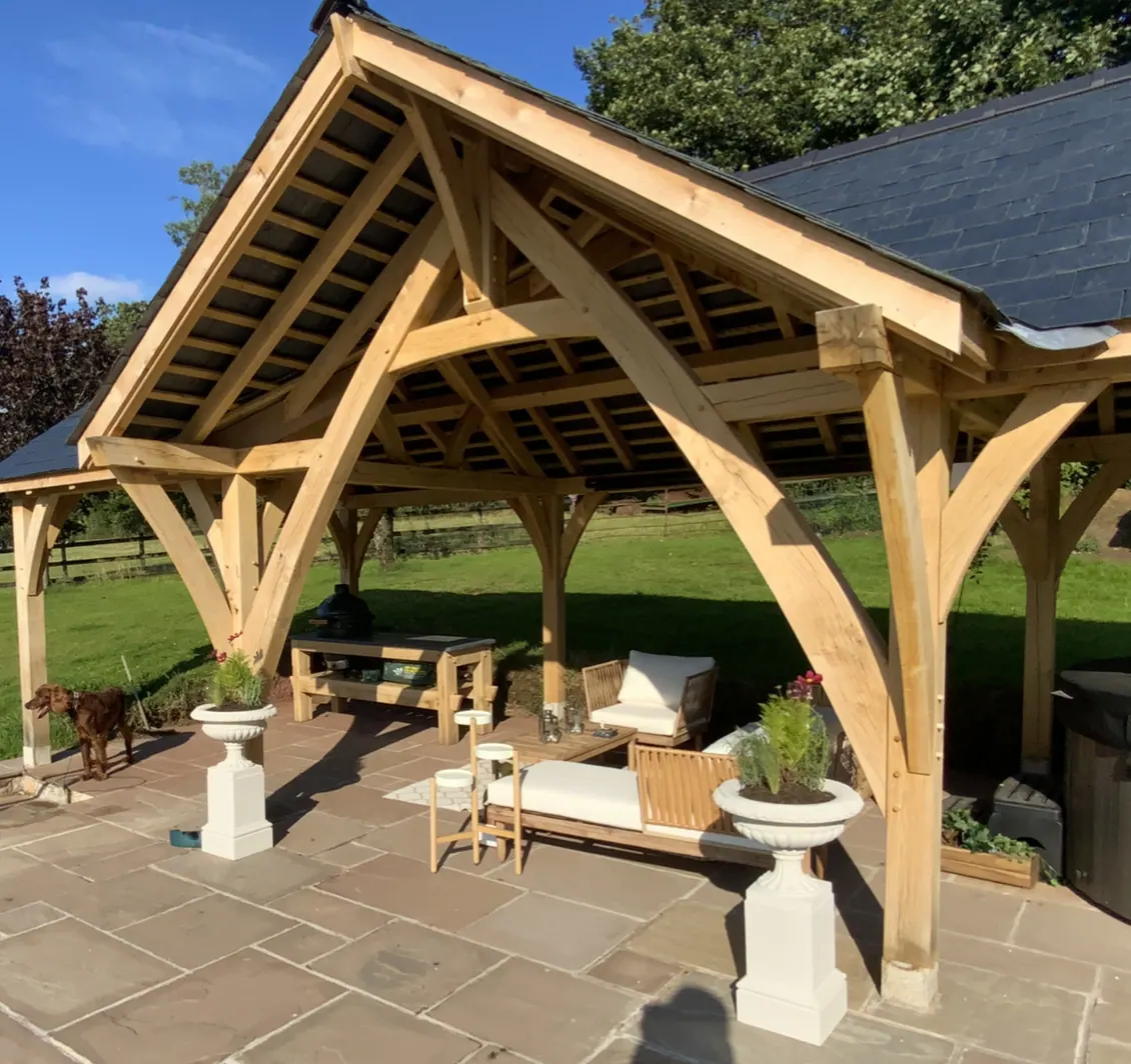 The oak garden pavilion at Devauden, its slate roof over a patio with outdoor seating.