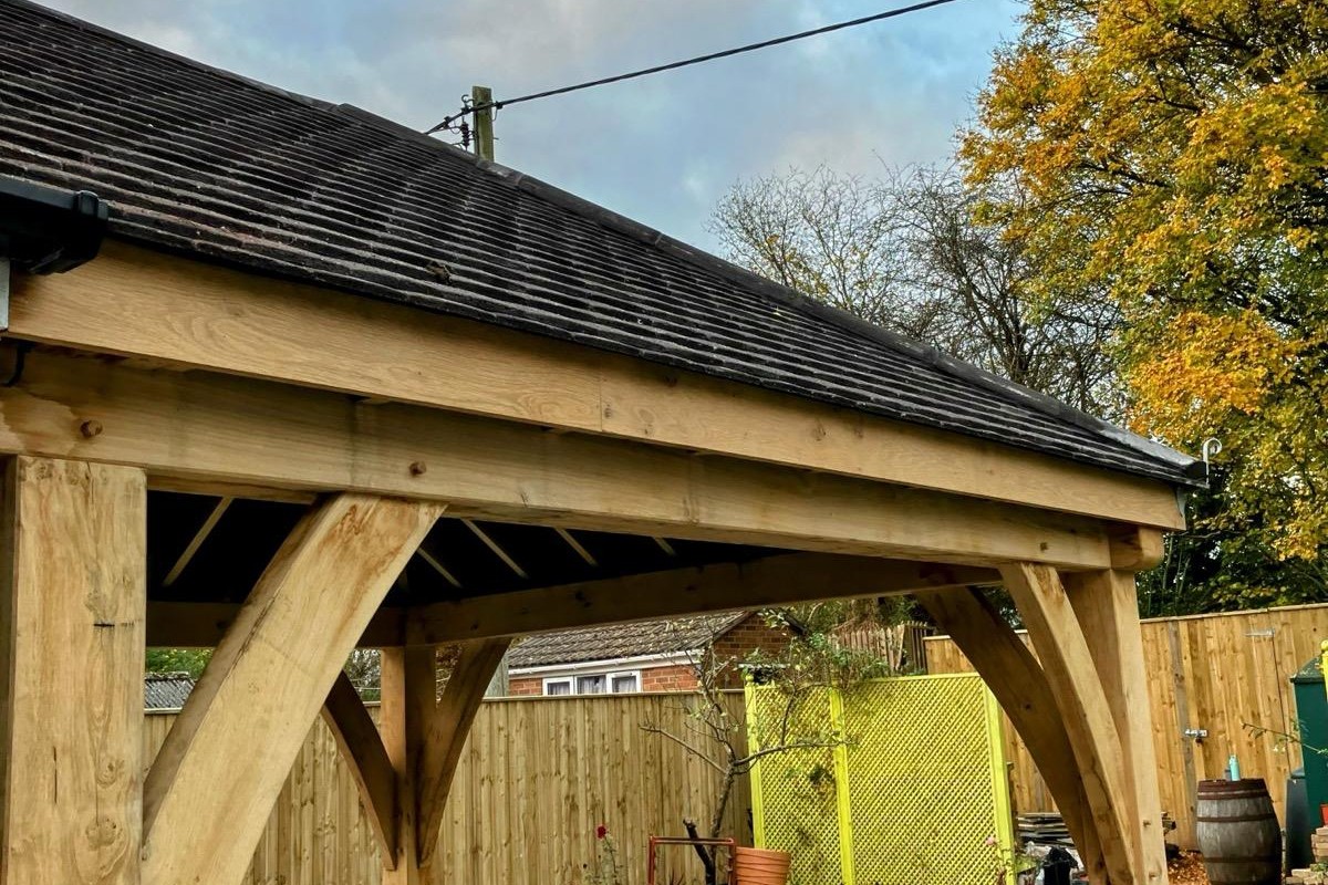 Oak frame gazebo with curved braces and a tiled hipped roof, against autumn trees at Gilwern