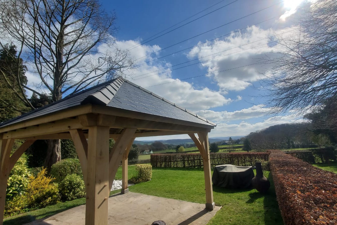 Oak frame gazebo with a hipped slate roof over a paved patio, looking out across the valley at Goytre.