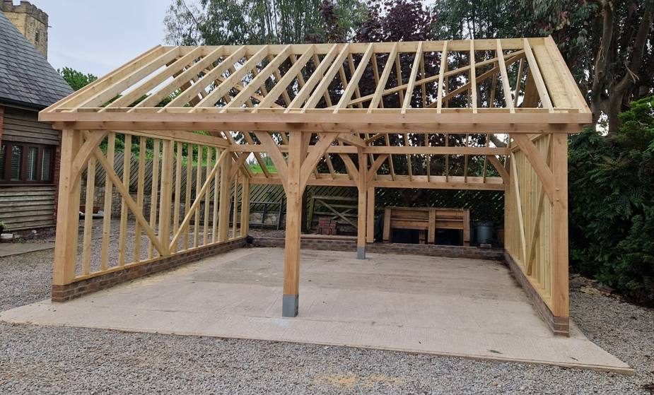 The oak frame of a two-bay garage raised on its slab, with the roof structure on and the wall studwork in place