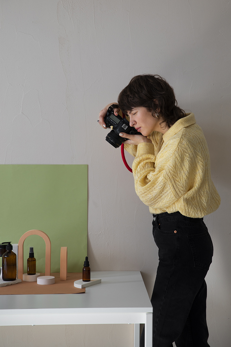 Freelance photographer shooting a styled product flat lay with amber glass bottles and geometric props against a green backdrop