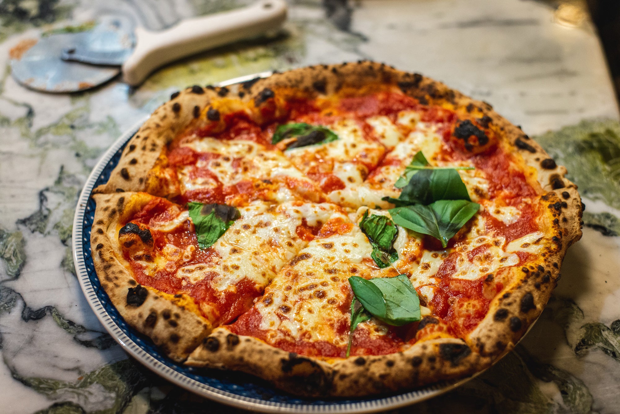 Margherita pizza with melted mozzarella, tomato sauce, and fresh basil on a blue-rimmed plate.
