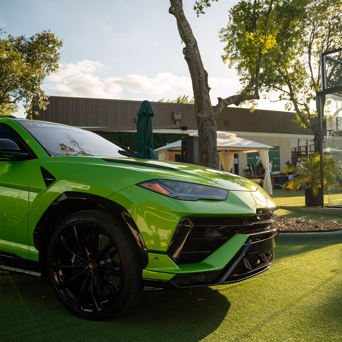 Front side view of a bright green Lamborghini parked on grass near trees and tents.