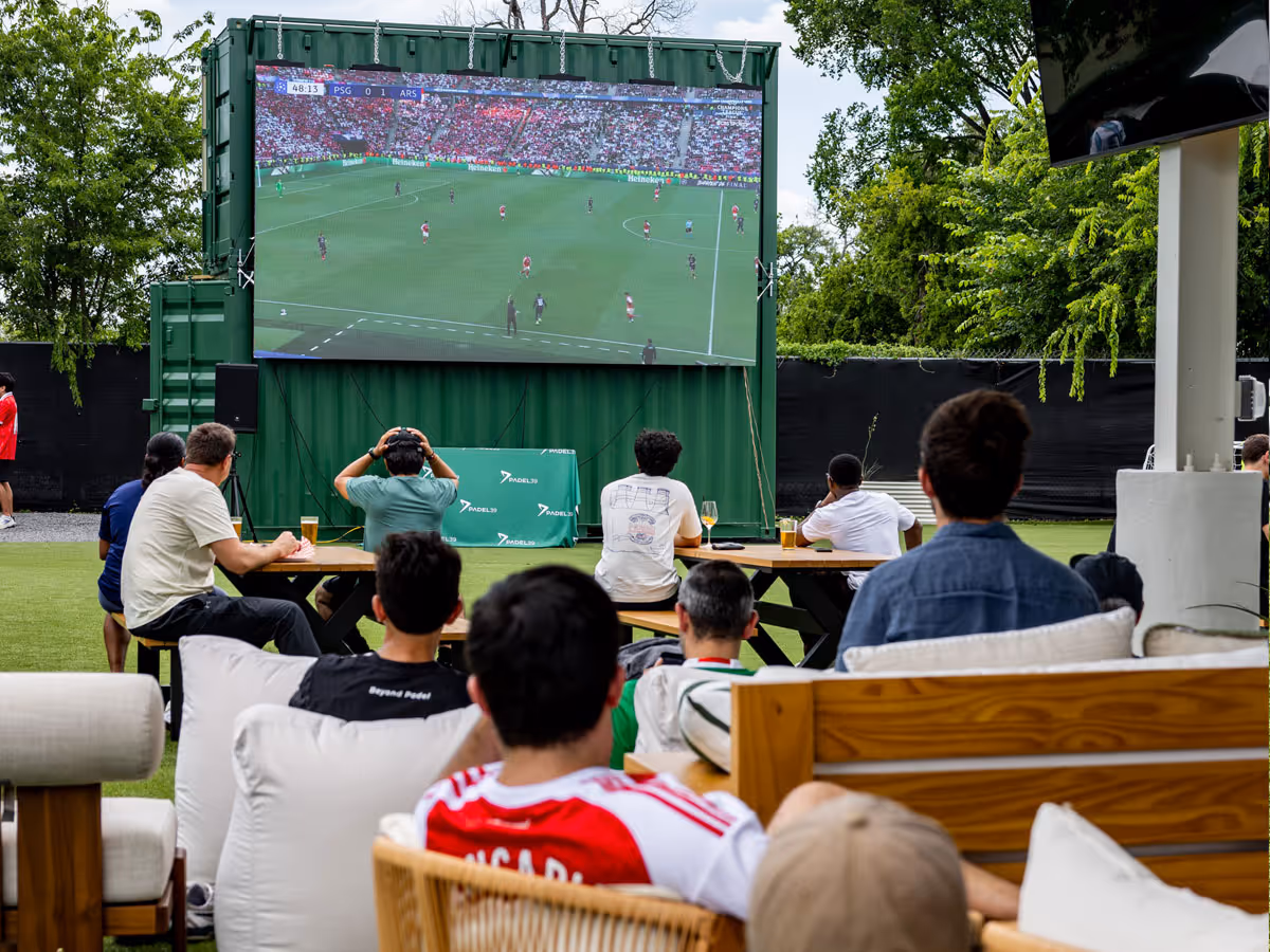 People seated outdoors watching a soccer match between PSG and Arsenal on a large screen.