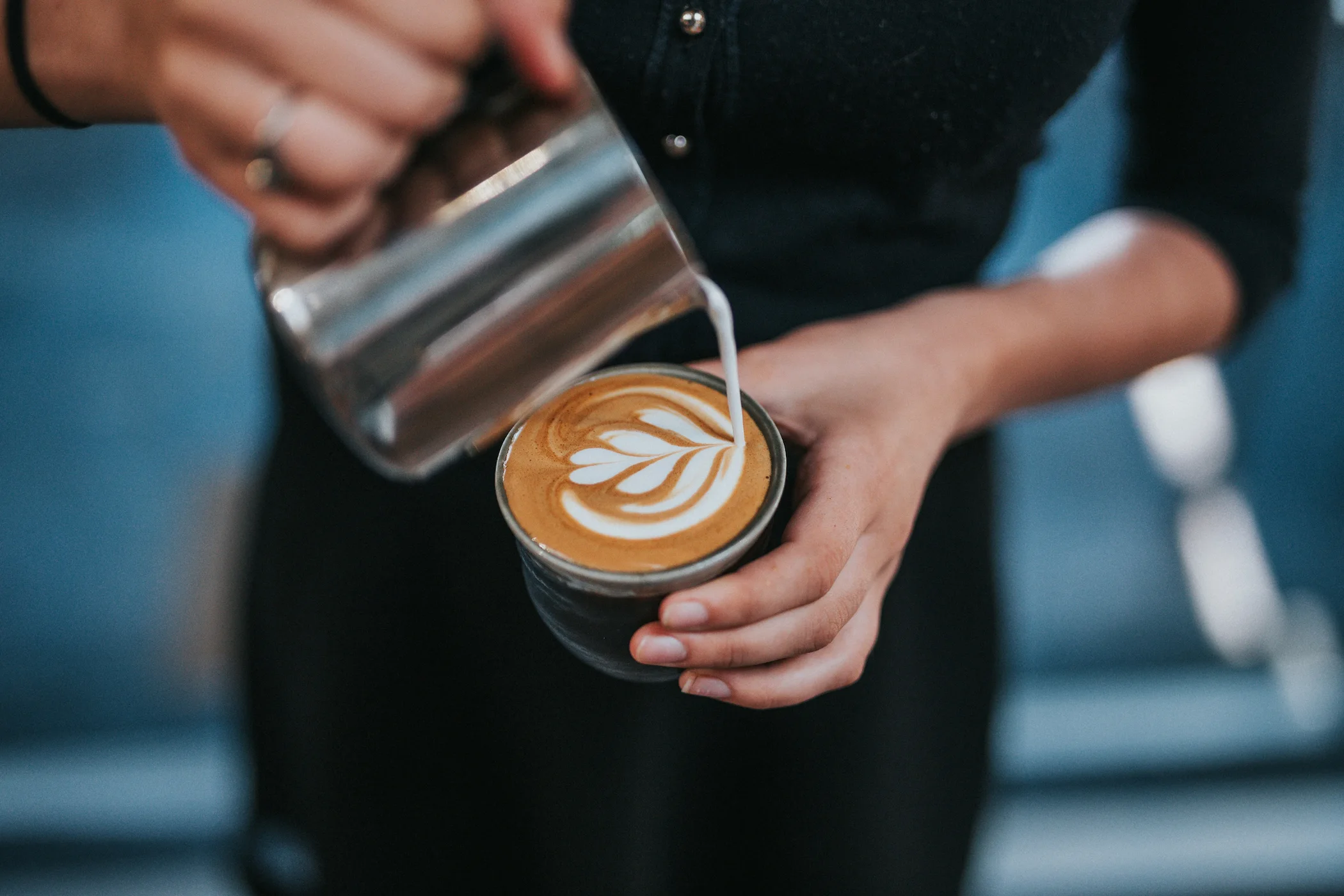 Person pouring steamed milk creating latte art in a cup of coffee.