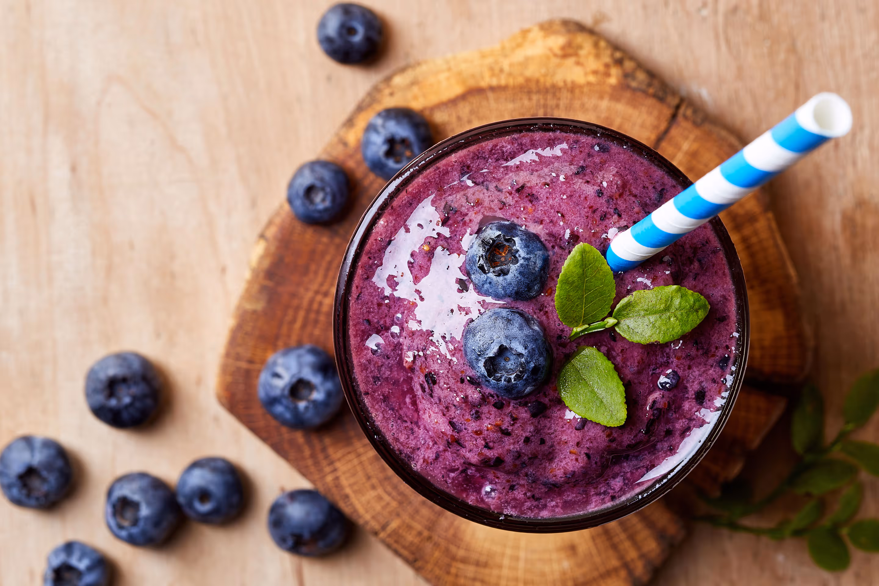 Top view of purple blueberry smoothie with fresh blueberries and mint leaves on wooden surface.