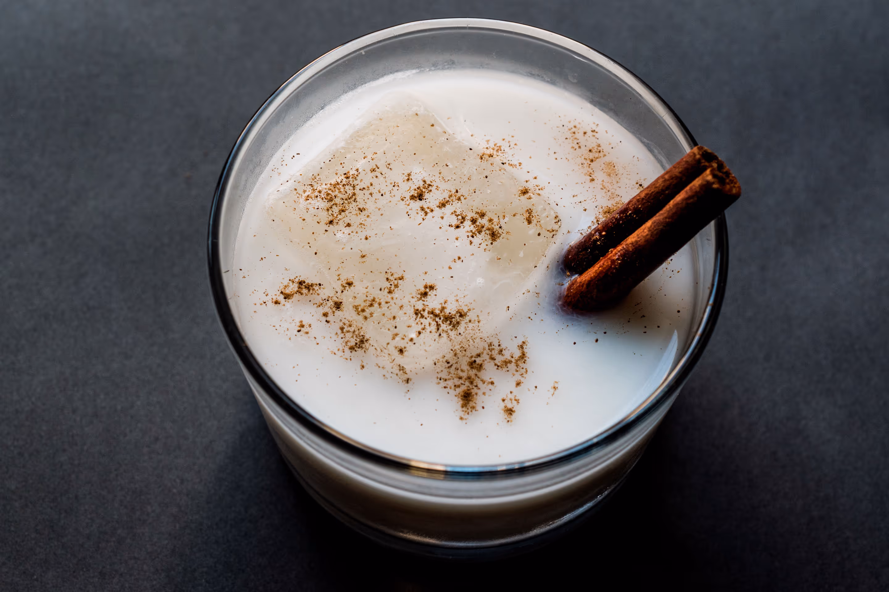 Glass of creamy horchata with ice cubes, cinnamon sticks, and ground cinnamon on top.