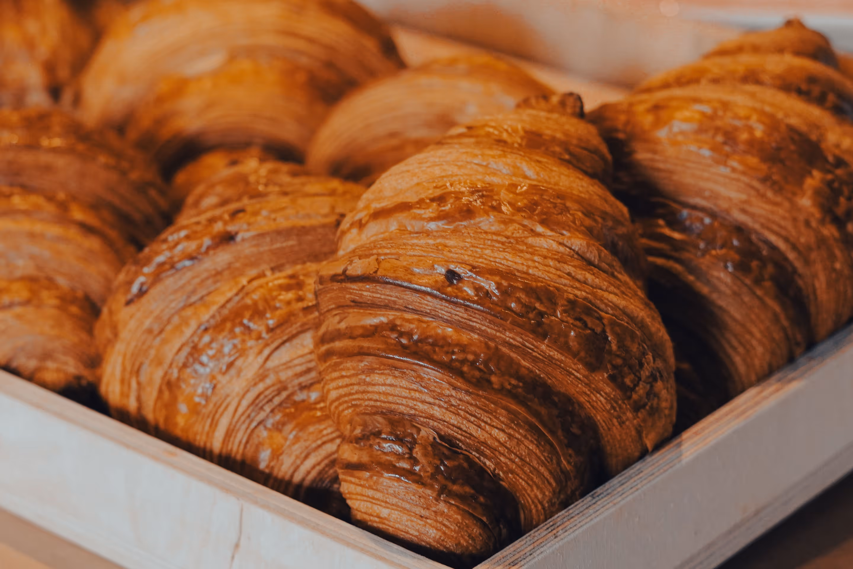 Freshly baked croissants arranged in a wooden crate, showing golden flaky layers.