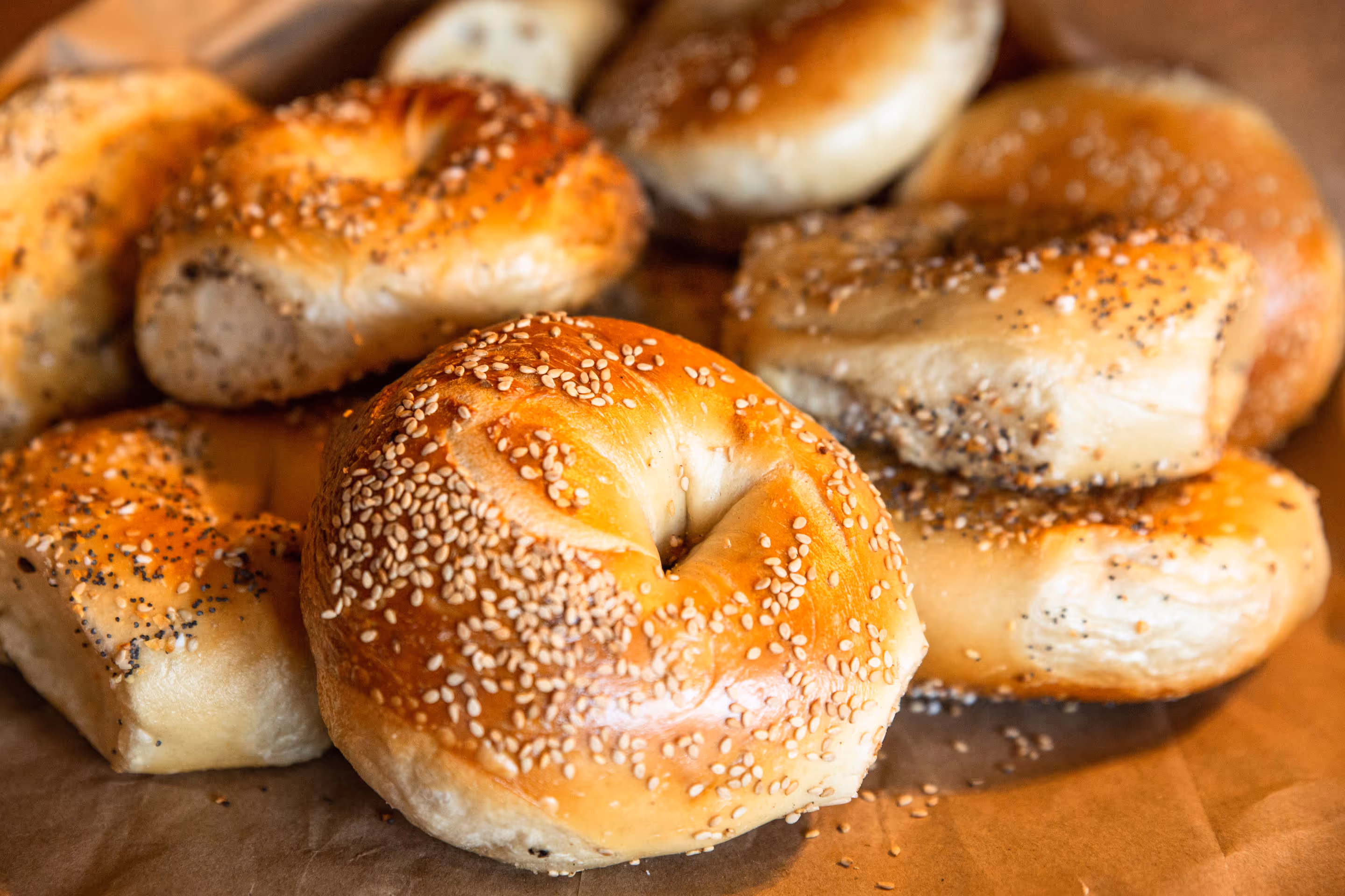 Several sesame and seed-topped bagels on brown parchment paper.