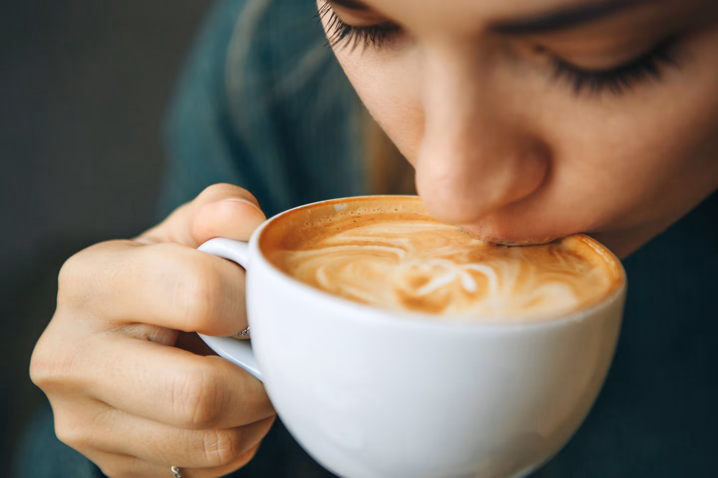Close-up of a person sipping a cappuccino with latte art in a white cup.