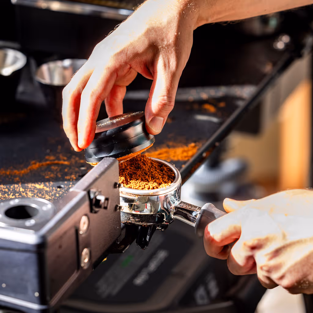 Roasted coffee beans pouring out of a black metal coffee roasting machine.