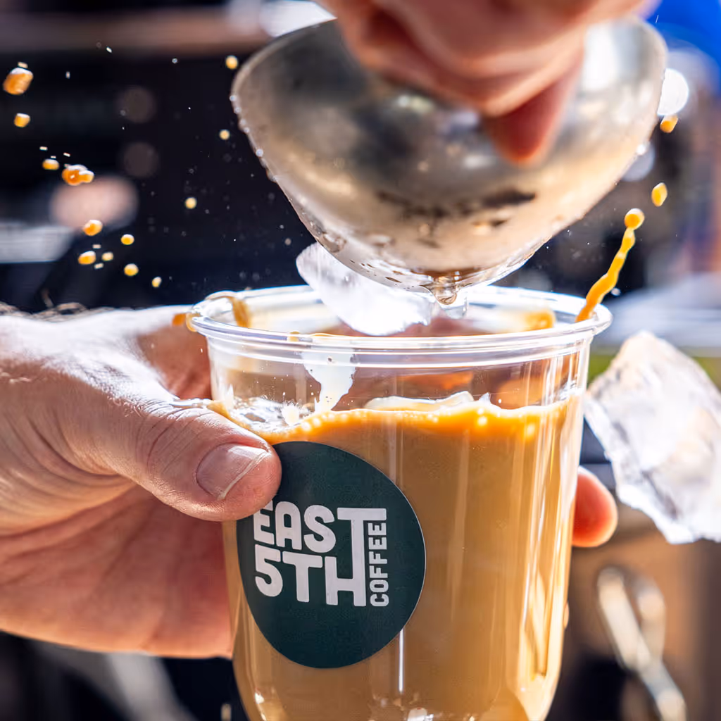 Person pouring steamed milk creating latte art in a cup of coffee.