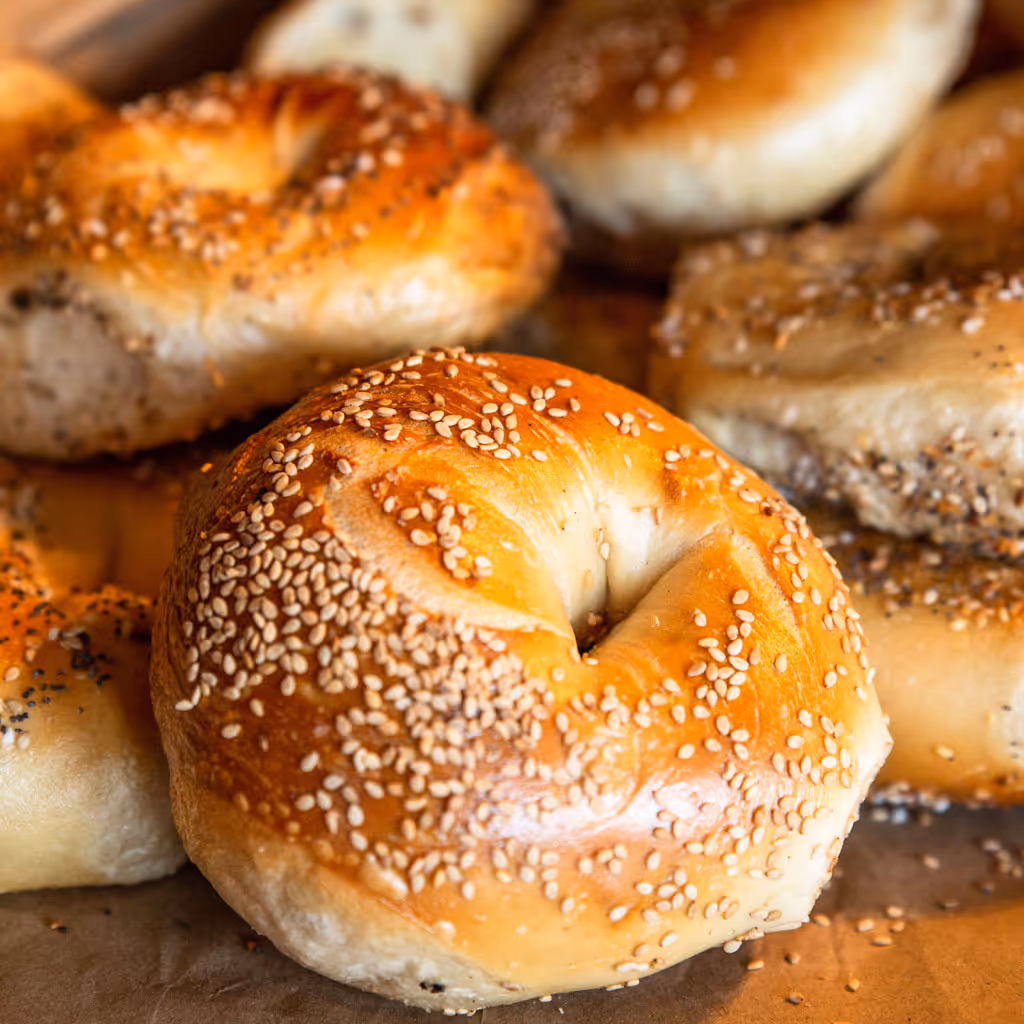 Several sesame and seed-topped bagels on brown parchment paper.