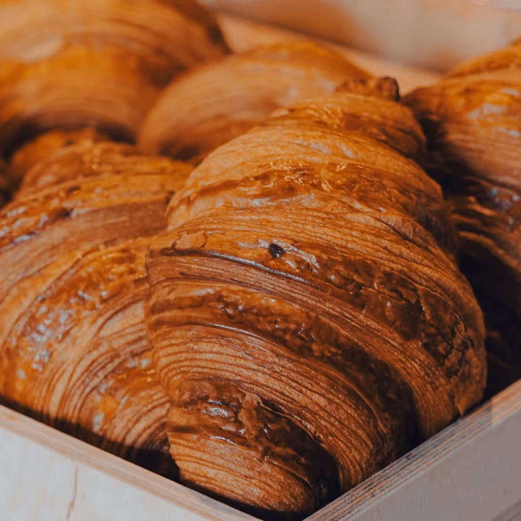 Freshly baked croissants arranged in a wooden crate, showing golden flaky layers.