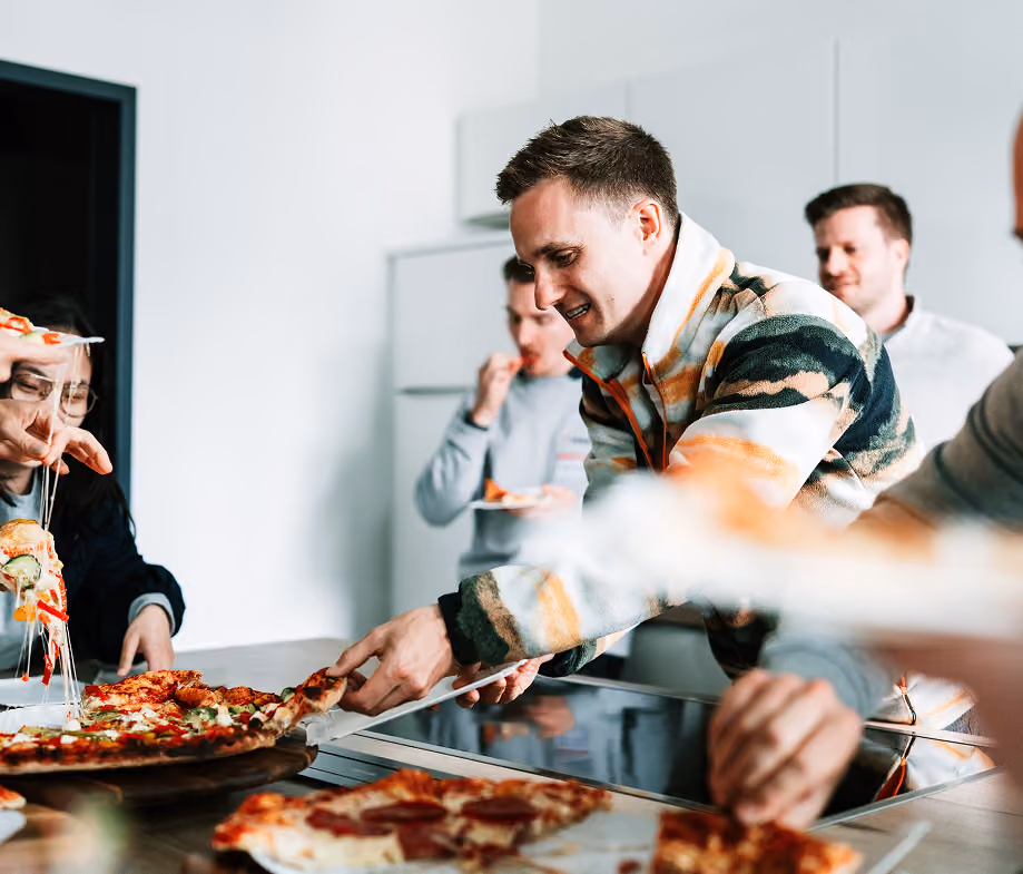 Lächelnde Menschen nehmen Pizzastücke in einer modernen Küche.