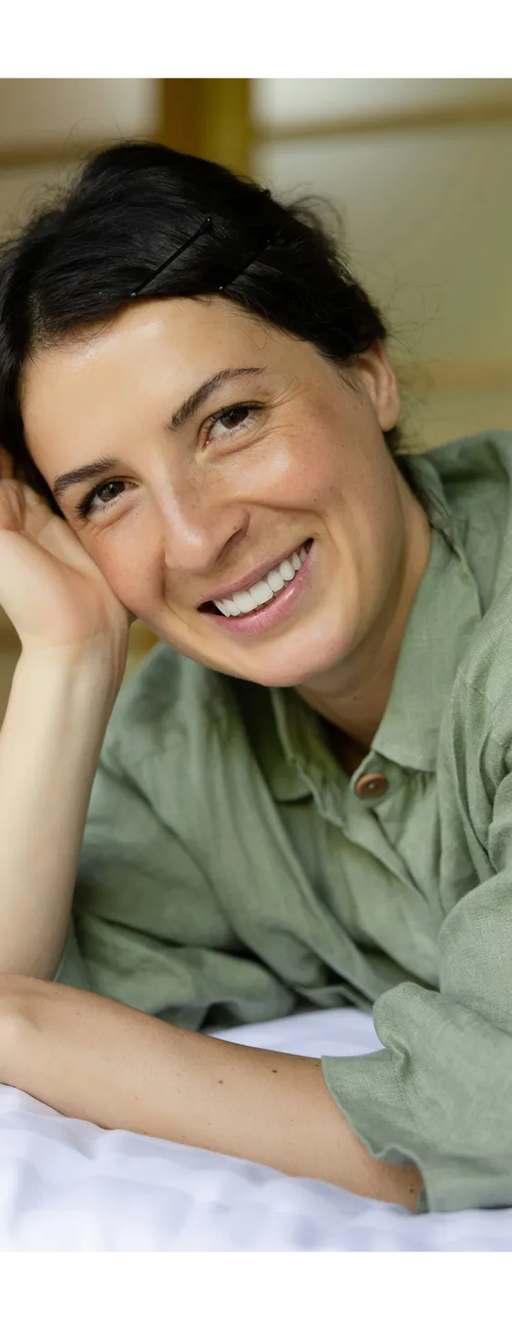 Smiling woman with dark hair pinned back wearing a green shirt, resting her head on her hand.
