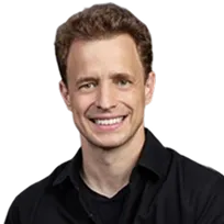 Smiling man with short curly brown hair wearing a black shirt on a transparent background.