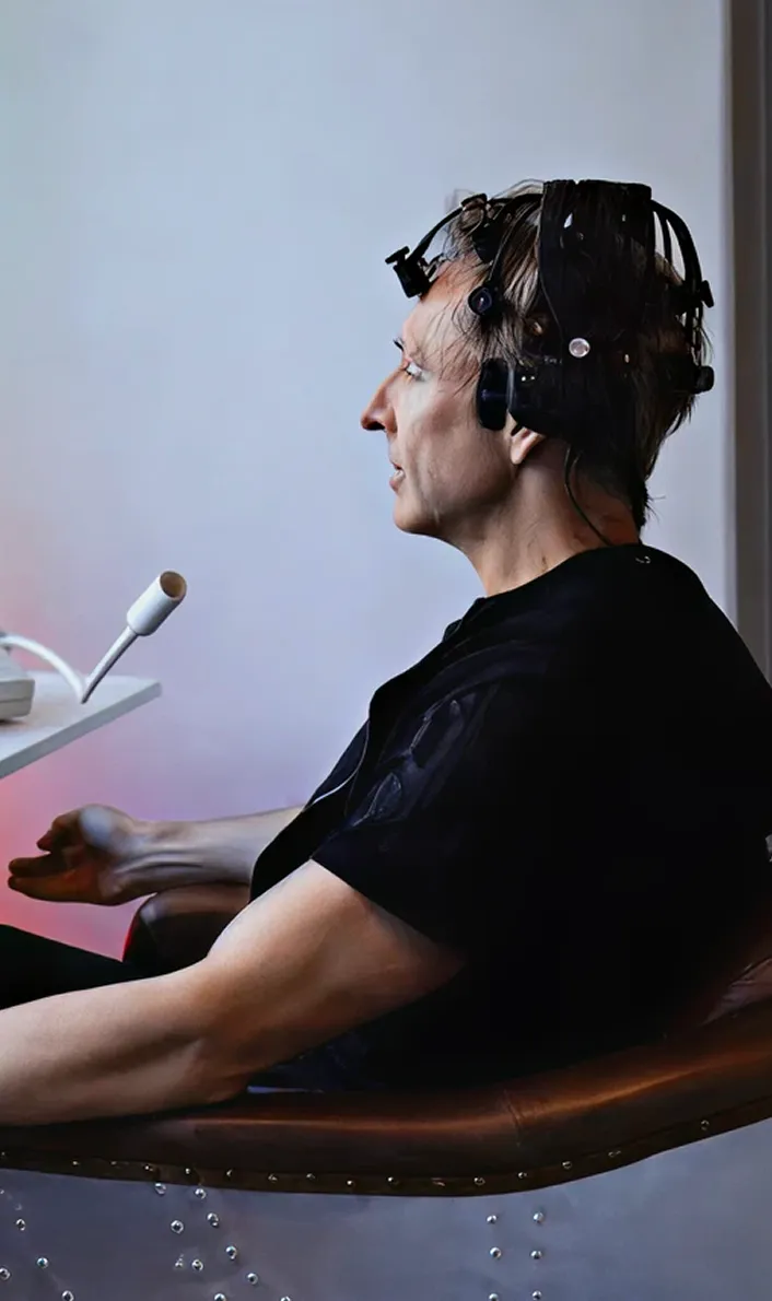 Man sitting sideways wearing a brainwave monitoring headset with sensors on his head.