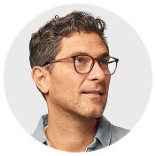 Portrait of a man with short curly hair and glasses looking to the side.