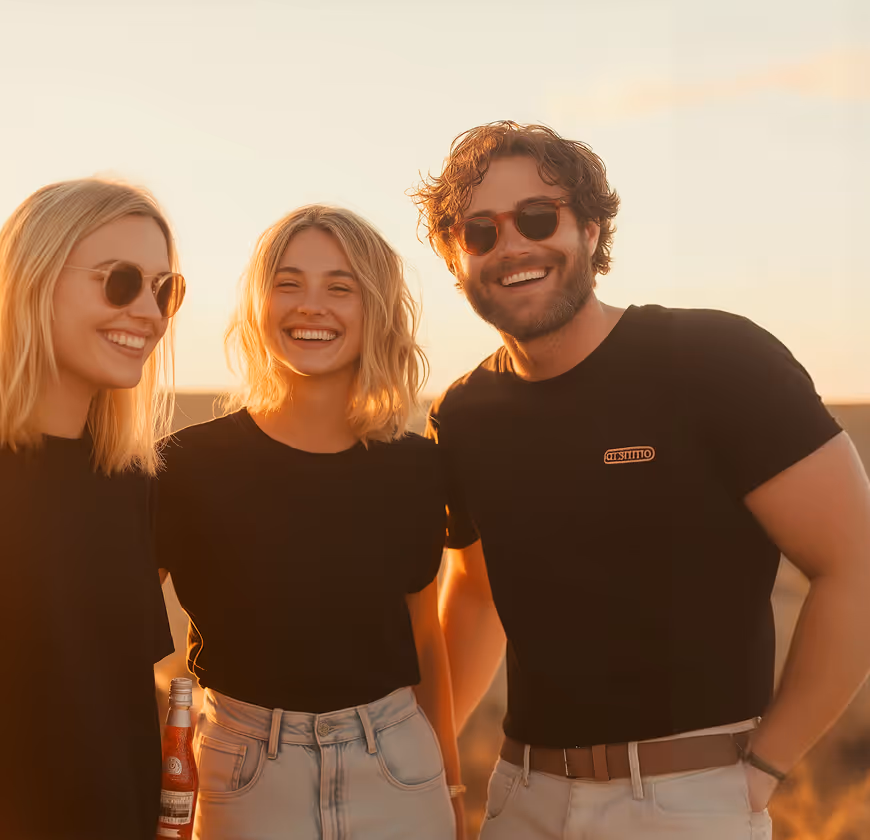 Three young adults smiling outdoors in casual clothes at sunset, two women and one man wearing sunglasses.