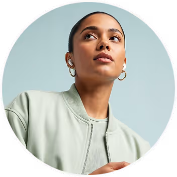 Young woman with hoop earrings and light jacket looking up against a pale blue background.