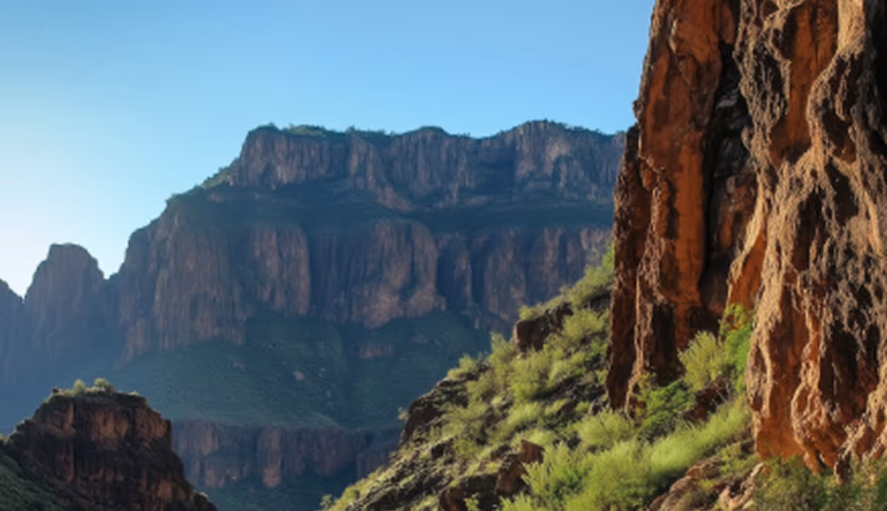 Rocky canyon cliffs with green shrubs under a clear blue sky during daylight.
