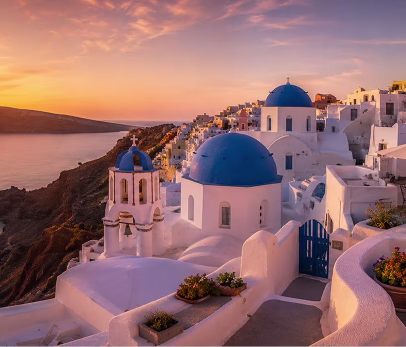 Sunset over Santorini with white buildings and iconic blue-domed churches by the sea.