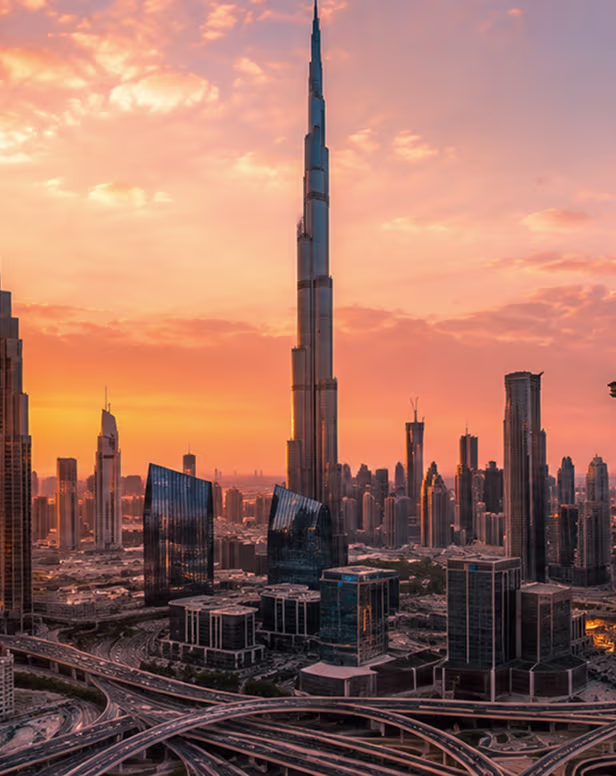 Dubai skyline at sunset featuring the Burj Khalifa and surrounding skyscrapers with highways below.