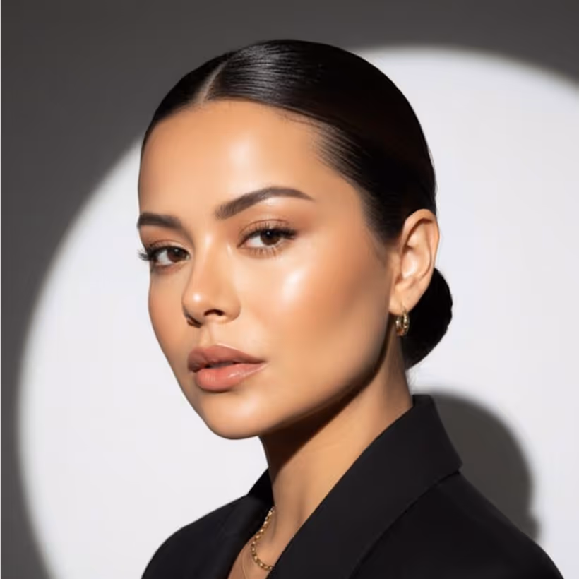 Portrait of a woman with sleek pulled-back hair, natural makeup, and gold hoop earrings against white background.