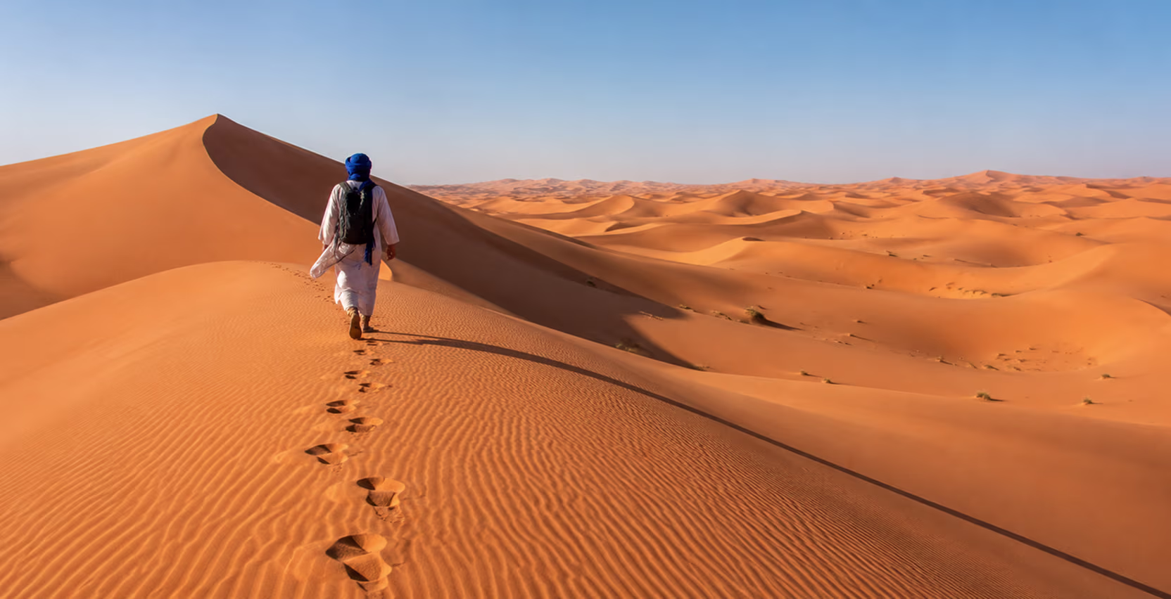 Traveler walking across Sahara desert dunes