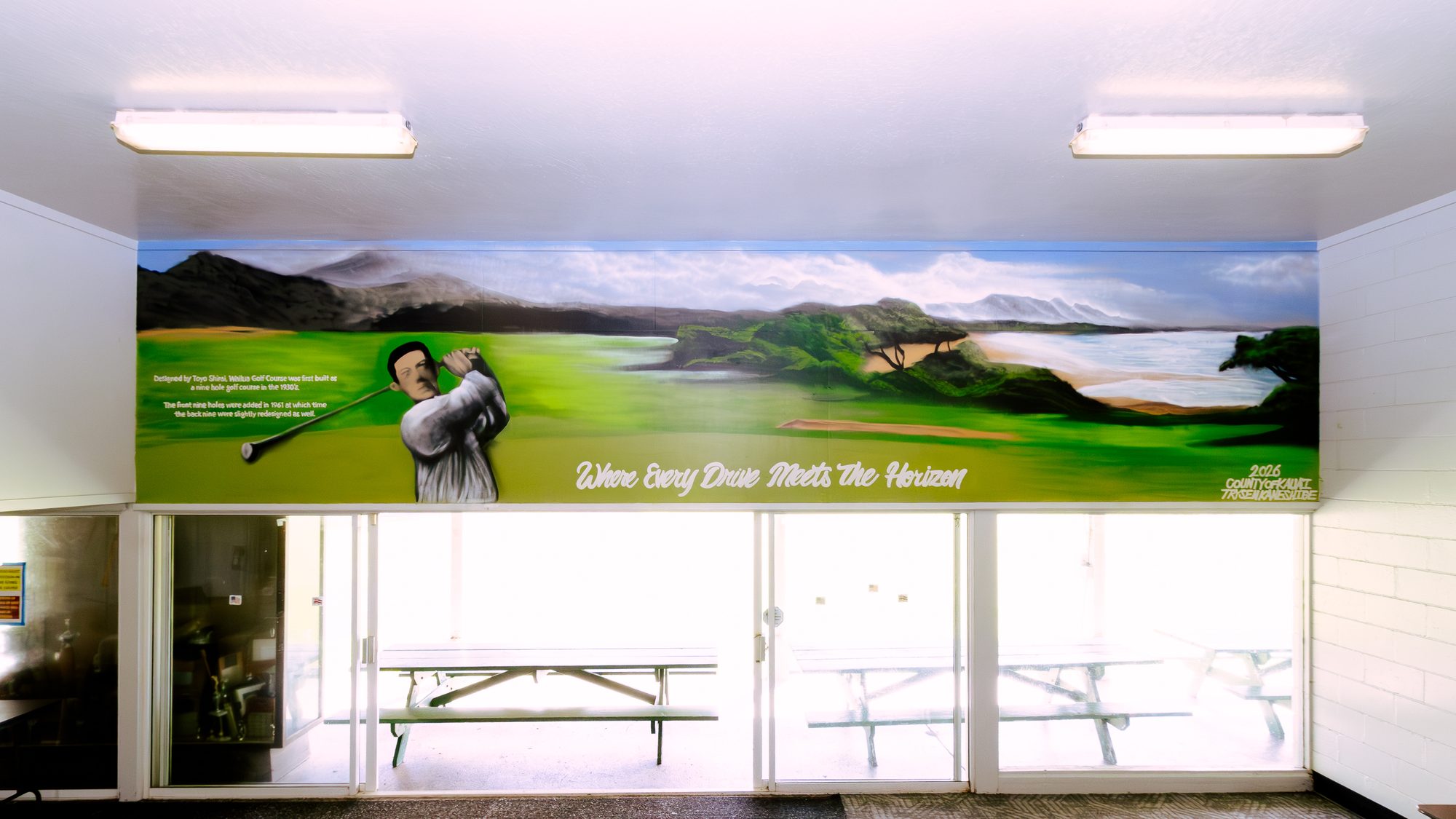 Wailua Golf Course clubhouse mural: course designer Toyo Shirai painted in black and white mid-swing beside a green fairway running to the coast, with his story lettered on the left and Where Every Drive Meets The Horizon below