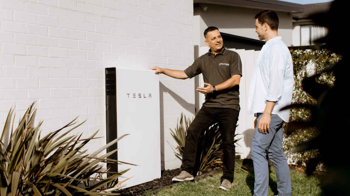 Homeowner discussing Tesla home battery system with solar consultant outside modern home.