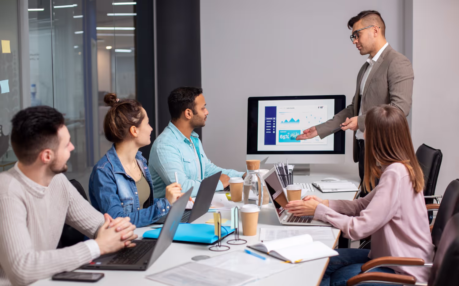 Business team attending a presentation with a man pointing at charts on a computer screen in a conference room.