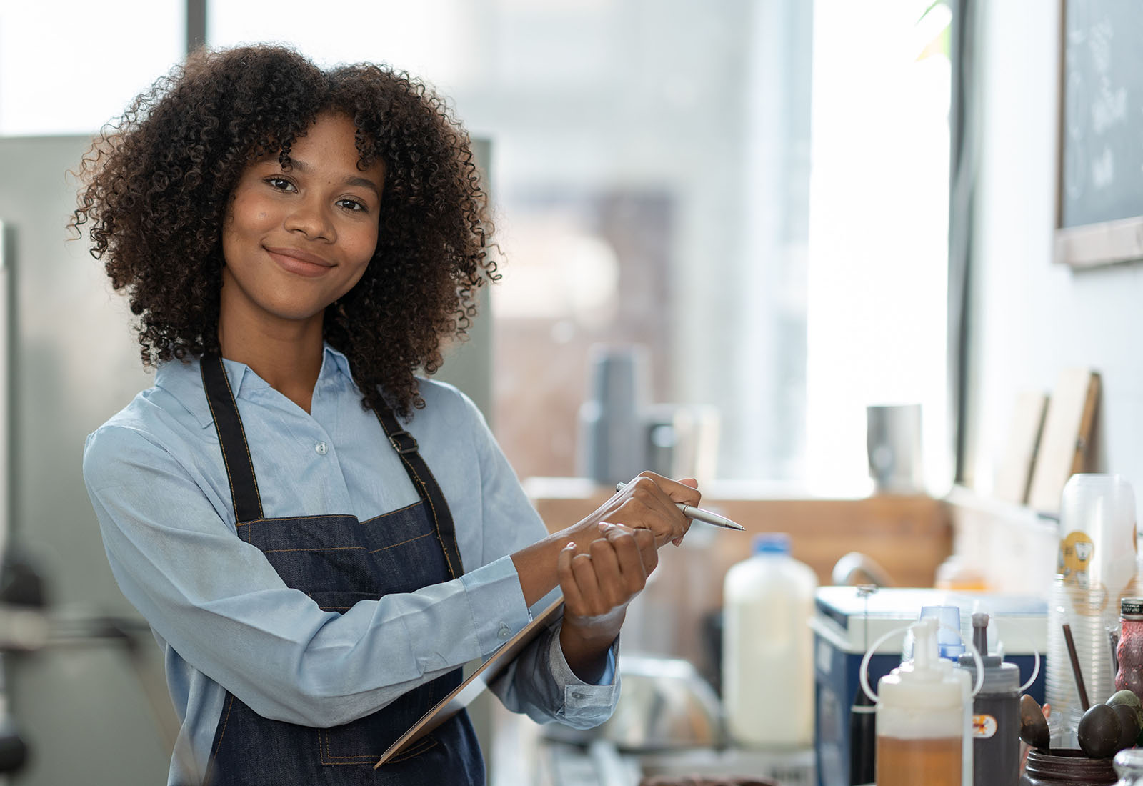 Café employee holding a clipboard and pen beside a counter with supplies