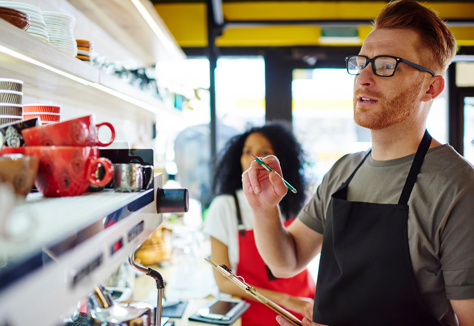 Shop worker in an apron reviewing shelf stock while a colleague records items nearby