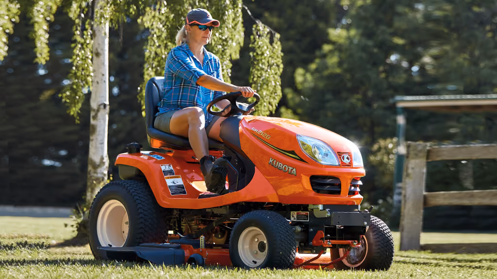 Person driving an orange Kubota ride-on mower across a lawn.