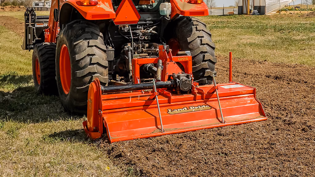 Orange rotary tiller attachment for breaking up soil.